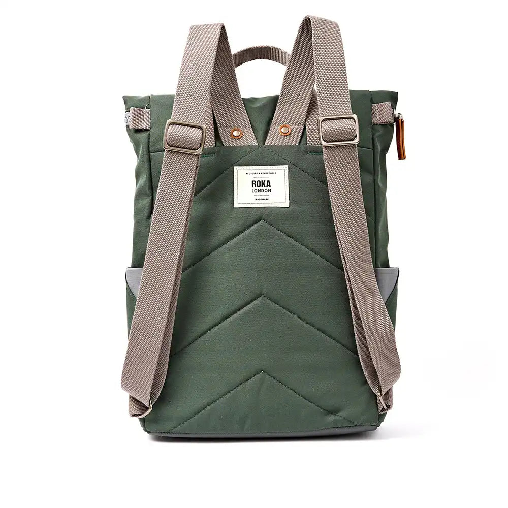 A back view of a dark olive green roll-top backpack with grey webbed shoulder straps, a white brand label reading 'ROKA', and a chevron quilted pattern, shown against a plain white background.