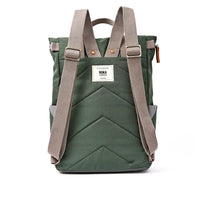 A back view of a dark olive green roll-top backpack with grey webbed shoulder straps, a white brand label reading 'ROKA', and a chevron quilted pattern, shown against a plain white background.