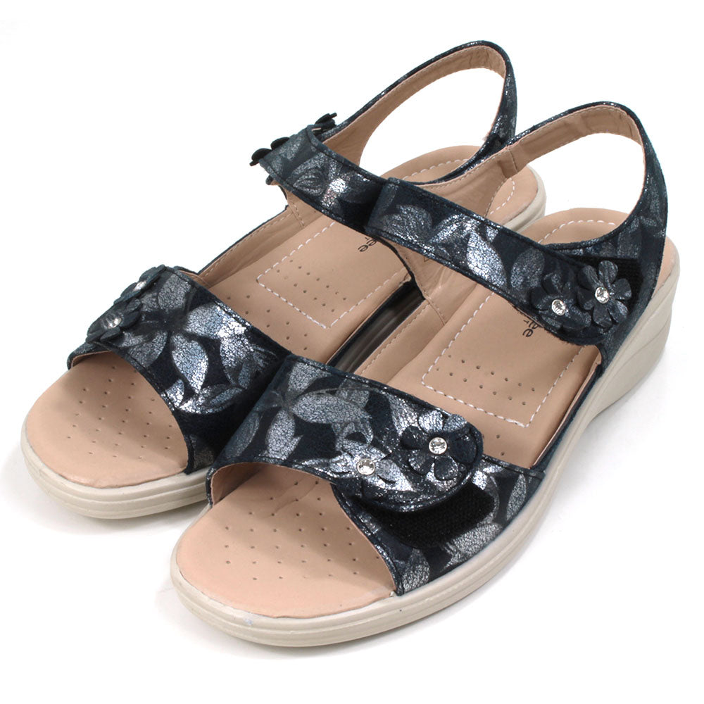 Navy sandals with floral pattern on fabric. Double straps across the feet fastened with Velcro. Straps around the ankles. Light tan, padded insoles. Low heels. Angled view.