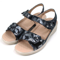 Shoe Tree Azalea navy sandals with floral pattern on fabric. Double straps across the feet fastened with Velcro. Straps around the ankles. Light tan, padded insoles. Low heels. Angled view.