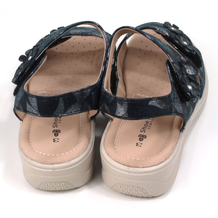 Navy sandals with floral pattern on fabric. Double straps across the feet fastened with Velcro. Straps around the ankles. Light tan, padded insoles. Low heels. Back view.