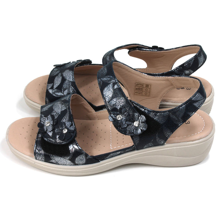 Navy sandals with floral pattern on fabric. Double straps across the feet fastened with Velcro. Straps around the ankles. Light tan, padded insoles. Low heels. Side view.