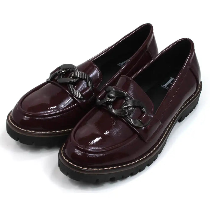 Shoes by Emma patent burgundy loafers with black chunky soles. Over the toes grey metal chain detail. Angled view.