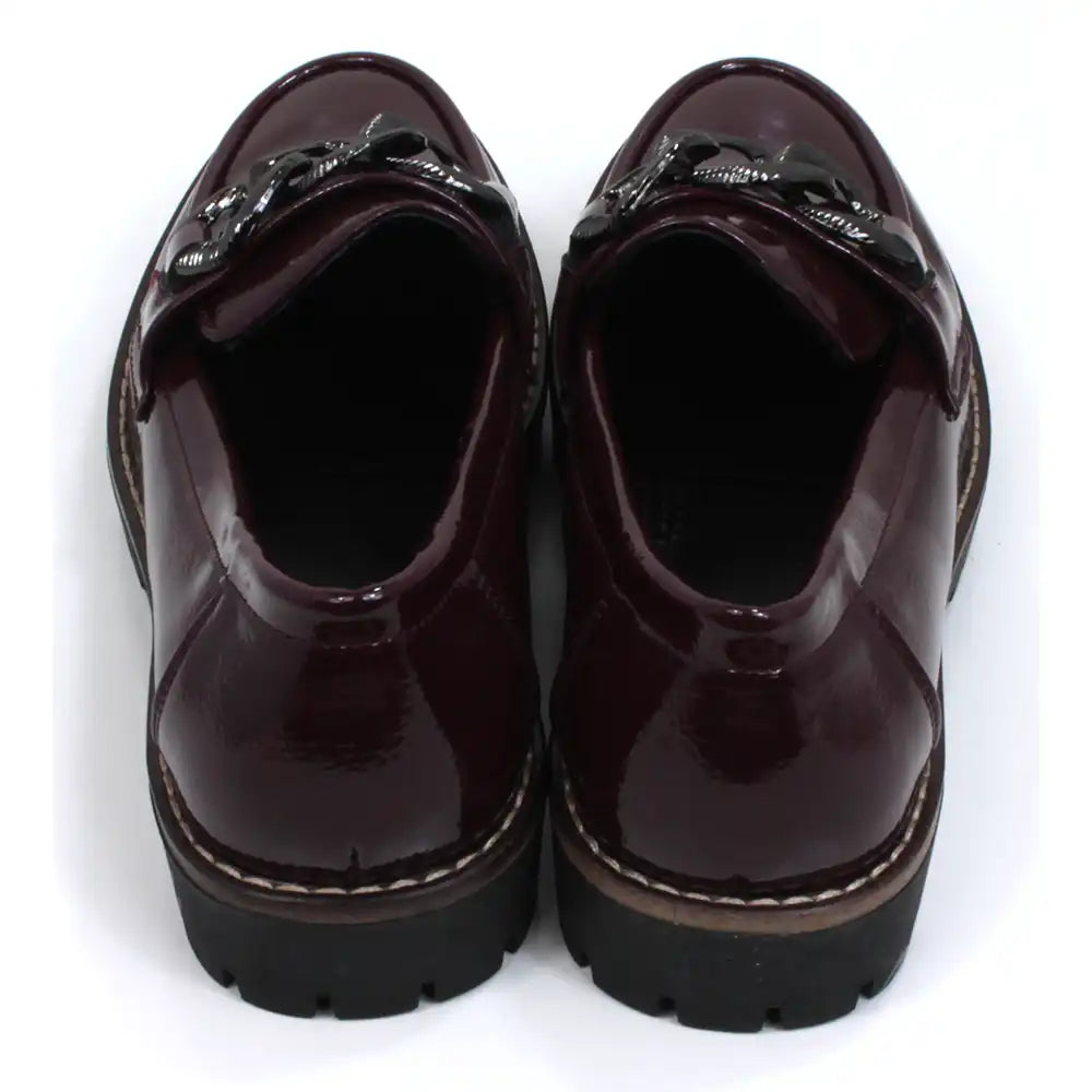 Shoes by Emma patent burgundy loafers with black chunky soles. Over the toes grey metal chain detail. Back view.