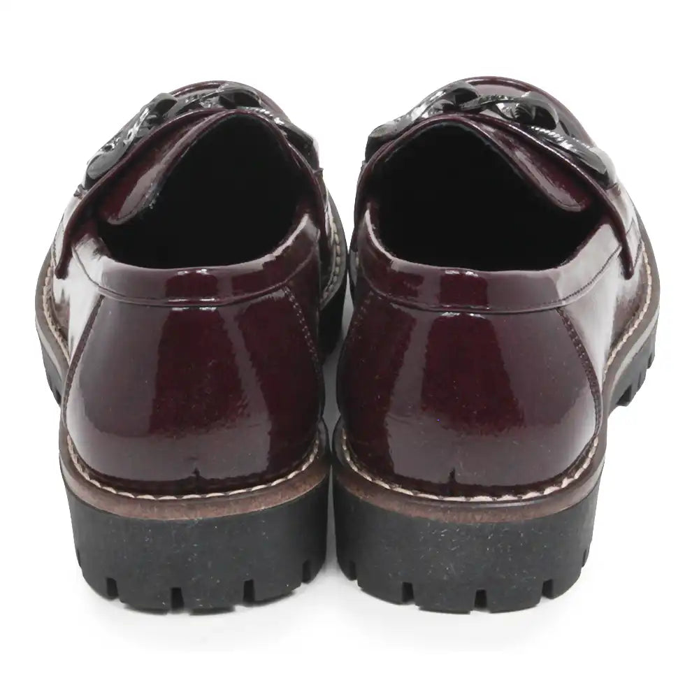 A pair of glossy patent leather loafers in deep burgundy, viewed from the back. They feature chunky black platform soles with white contrast stitching along the edge.