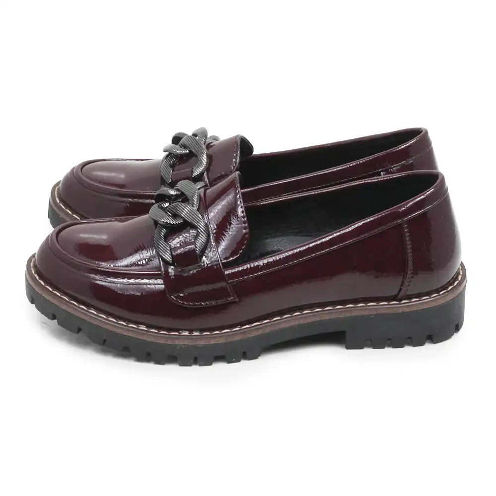 A pair of glossy burgundy leather penny loafers with chunky black chain details across the vamp and black lug soles, shown on a plain white background.