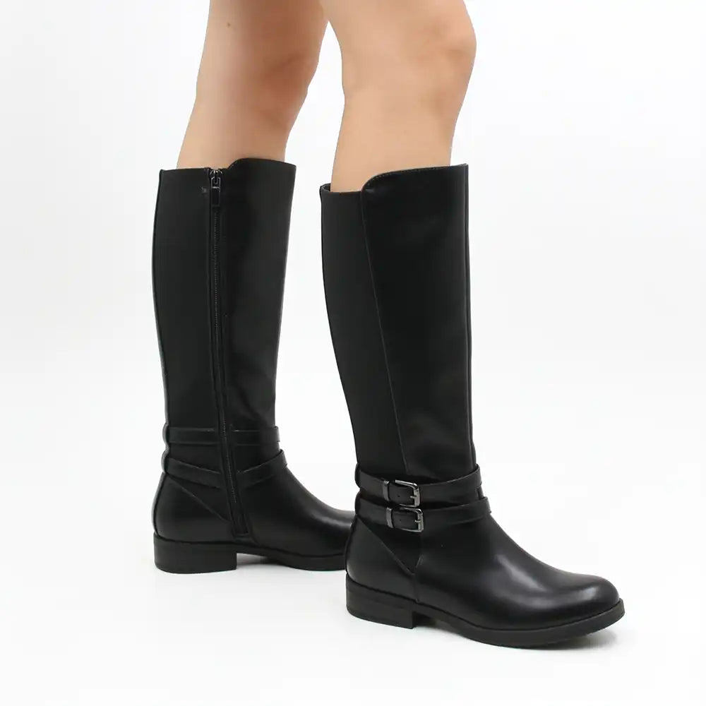 A pair of black knee-high leather boots with side zippers and buckle straps, shown on a model's feet against a white studio background.
