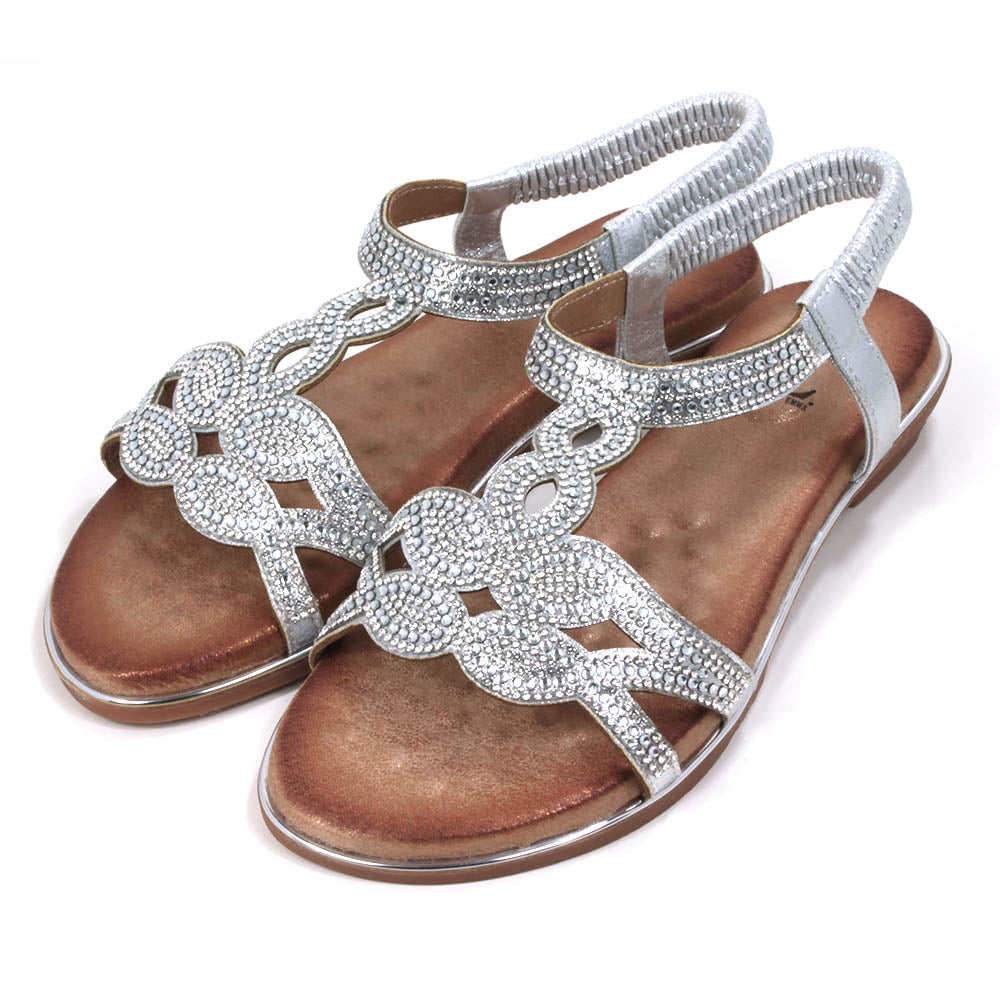 Emma silver, diamante covered sandals. Silver elasticated ankle straps. Tan coloured insoles. Silver trim around the soles. Angled view.