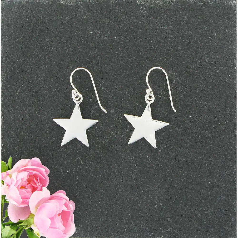 Silver star earrings on a dark slate surface with pink flowers.