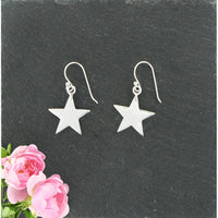 Silver star earrings on a dark slate surface with pink flowers.