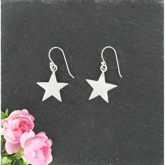 Silver star earrings on a dark slate surface with pink flowers.