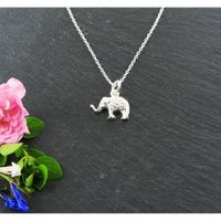 Silver elephant pendant necklace on a dark surface with pink flowers and green leaves.