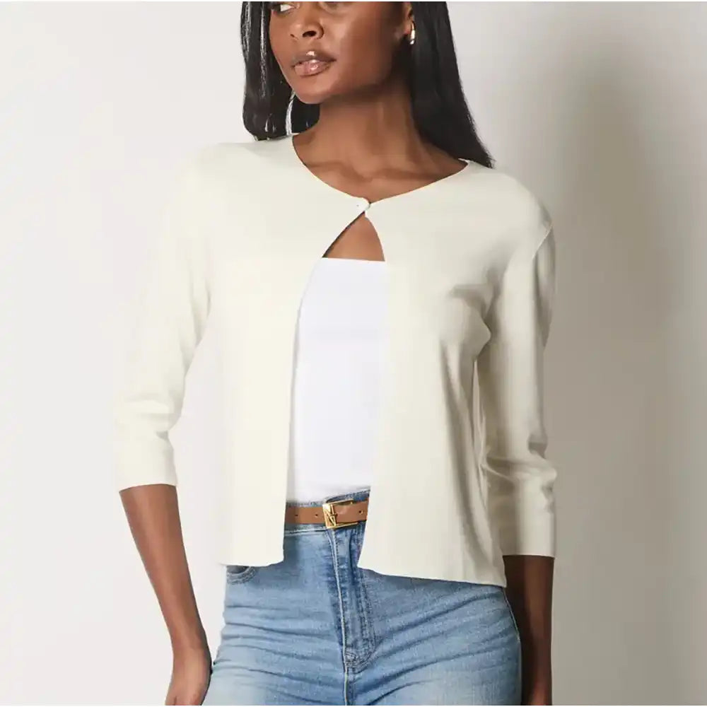 Woman wearing a white cardigan over a white top and blue jeans on a plain background