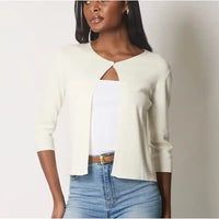 Woman wearing a white cardigan over a white top and blue jeans on a plain background