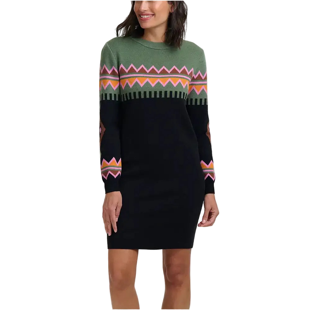 A woman wearing a long-sleeve knit sweater dress with a black body, green yoke, and colorful geometric pattern across the chest and sleeves, photographed against a plain light gray studio background.