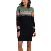 A woman wearing a long-sleeve knit sweater dress with a black body, green yoke, and colorful geometric pattern across the chest and sleeves, photographed against a plain light gray studio background.