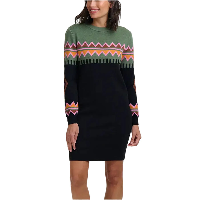 A woman wearing a long-sleeve knit sweater dress with a black body, green yoke, and colorful geometric pattern across the chest and sleeves, photographed against a plain light gray studio background.