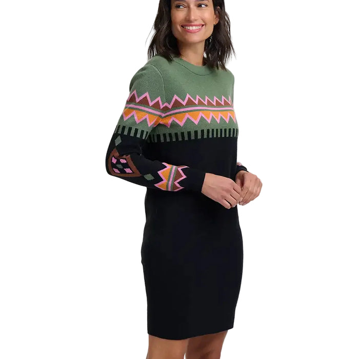 A woman wearing a long-sleeve knit sweater dress with a black body, olive green yoke, and a colorful geometric pattern across the chest and sleeves, photographed against a light gray studio background.