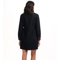 A woman viewed from the back wearing a black long-sleeve mini dress with a gathered waist and side slits, photographed against a plain white studio background.