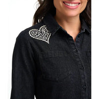 A close-up of a woman wearing a black denim button-up shirt with a white embroidered heart design on the left shoulder, set against a plain white background.