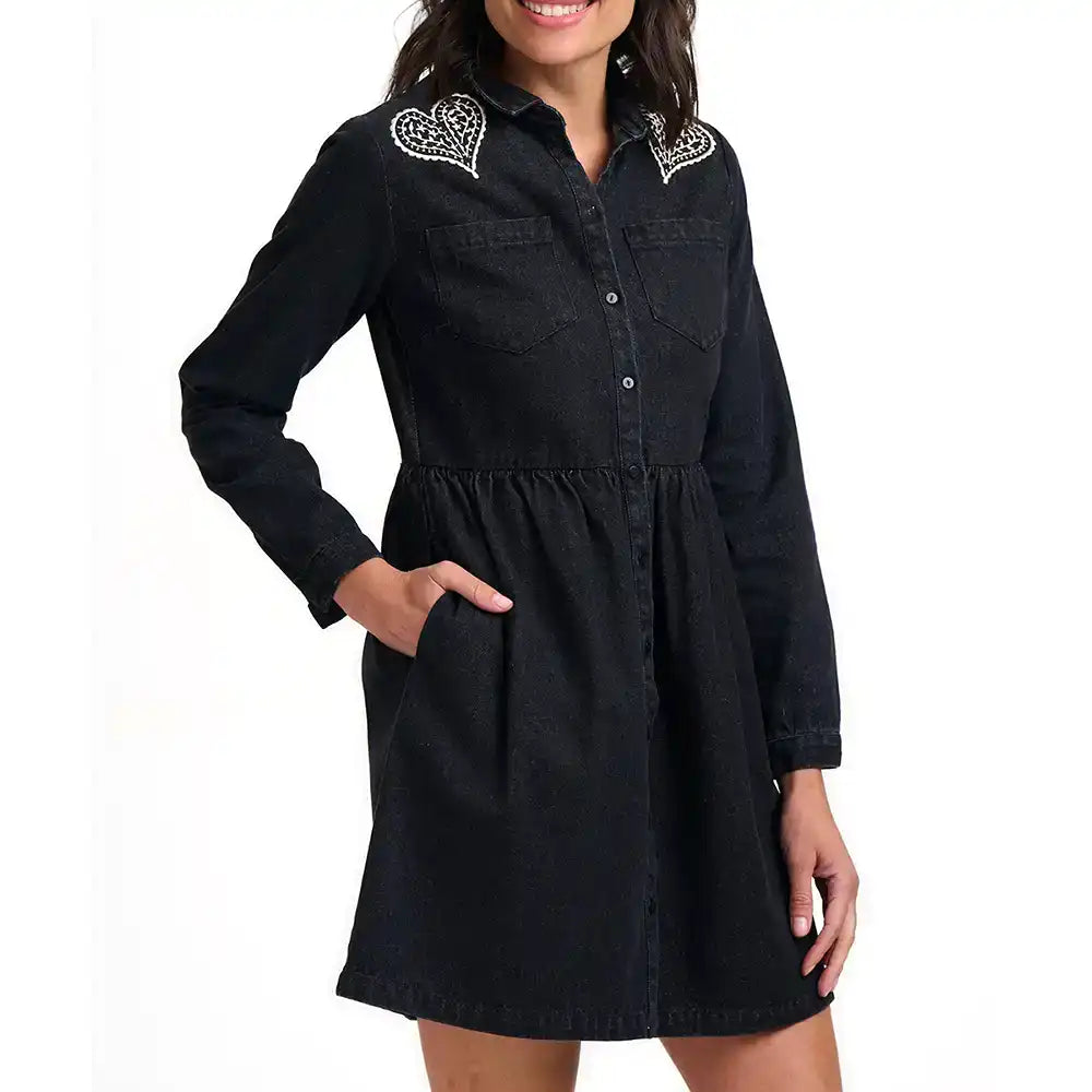 A woman wearing a black denim long-sleeve shirt dress with white embroidered heart details on the shoulders, shown against a plain white background.