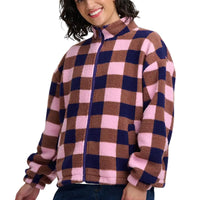 A woman wearing a fuzzy zip-up fleece jacket with a pink, brown, and navy blue checkered pattern, shown from the waist up against a white background.