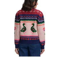 A woman shown from the back wearing a colorful knit sweater with two green swan motifs across the center and geometric pattern bands, paired with blue jeans against a plain light background.