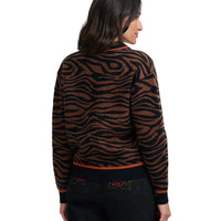 Woman with her back to the camera wearing brown and black tiger print bomber jacket in a white studio environment.