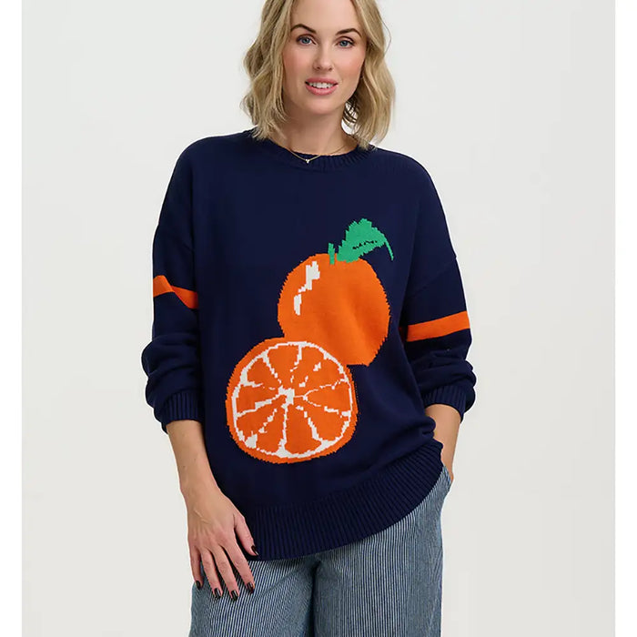 Woman wearing a navy sweater with orange and white graphics on a plain background