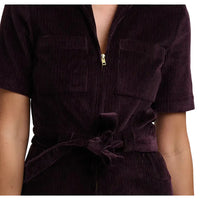 Woman wearing a short sleeved, cropped leg dark plum coloured, zip-up  boilersuit in a white studio environment. Close up showing belt, pockets and fabric.