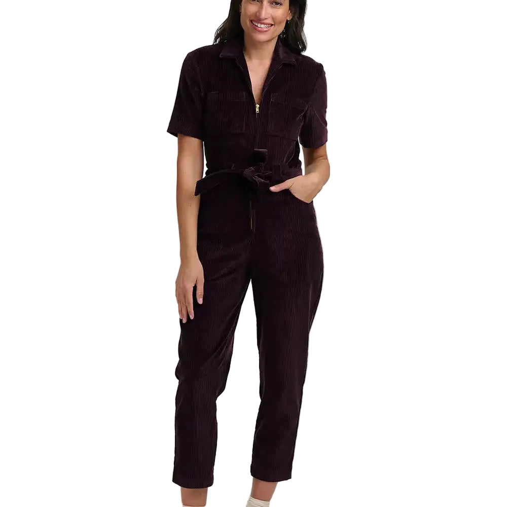 Woman wearing a short sleeved, cropped leg dark plum coloured, zip-up  boilersuit in a white studio environment.