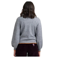 Woman wearing grey cardigan in a white studio environment. She has her back to the camera.