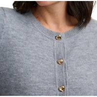 Woman wearing grey cardigan with gold heart shaped buttons in a white studio environment. Close up of the fabric and buttons.