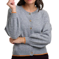 Woman wearing grey cardigan with gold heart shaped buttons in a white studio environment.