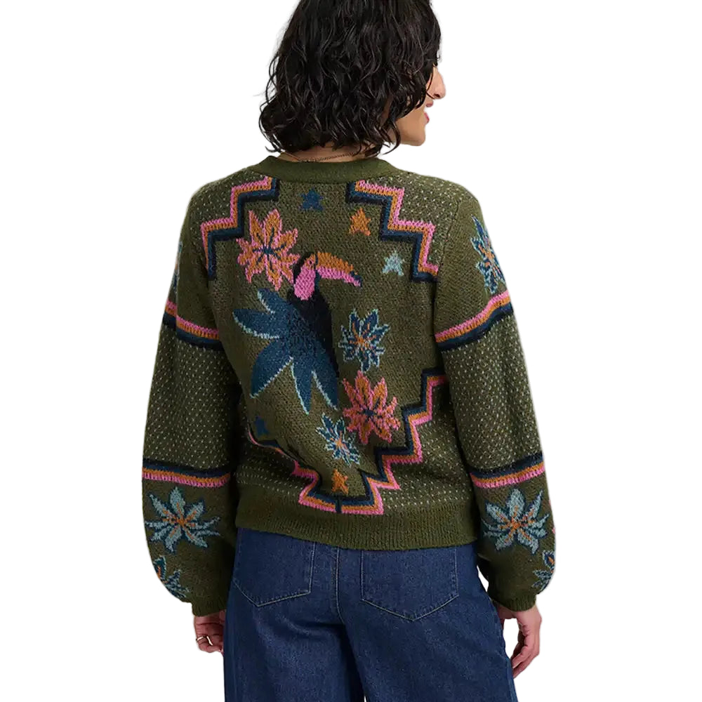 Woman wearing khaki green four button cardigan with flowers and toucans pattern. She is in a white studio environment. She has her back to the camera.
