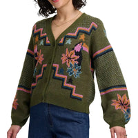 Woman wearing khaki green four button cardigan with flowers and toucans pattern. She is in a white studio environment.