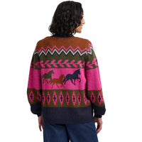 Woman wearing a multi coloured cardign with a running horses motif. She is facing away from the camera. She is in a white studio environment.