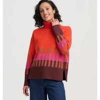 A woman modeling a bright orange turtleneck sweater with a brown and pink geometric stripe pattern across the chest and sleeves, paired with blue jeans against a white background.