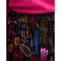 Back view of high-waisted, A-line midi skirt featuring a vibrant, multicolored botanical and bird pattern on a black background, showing elastication.