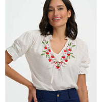 Woman wearing a white blouse with floral embroidery on a plain background
