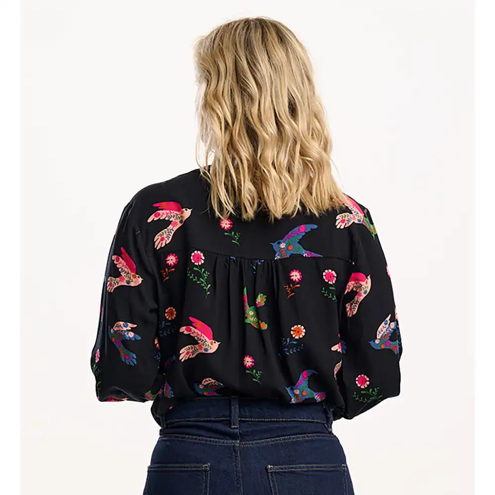 Person wearing a black blouse with colorful floral patterns on a white background