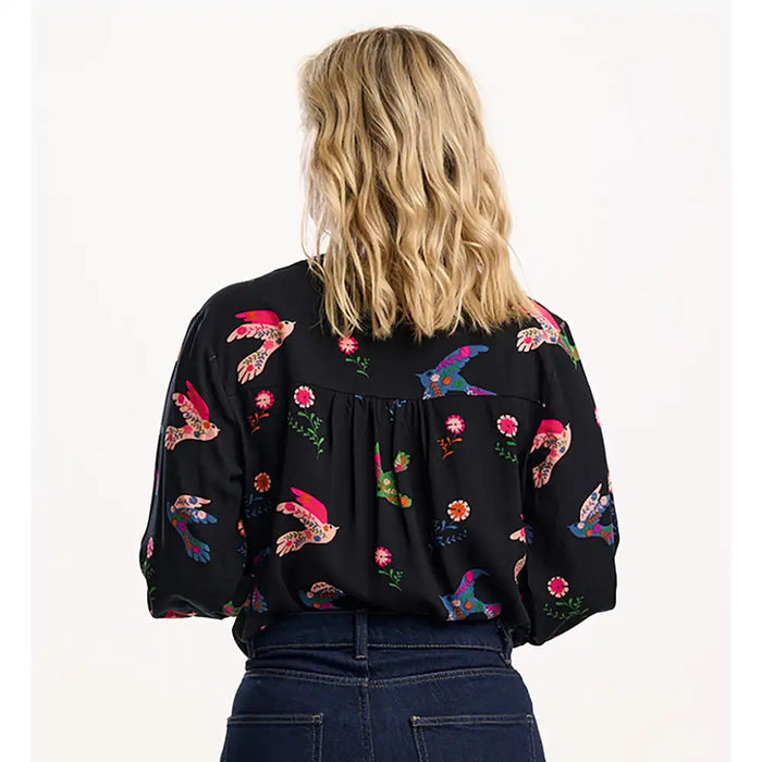 Person wearing a black blouse with colorful floral patterns on a white background