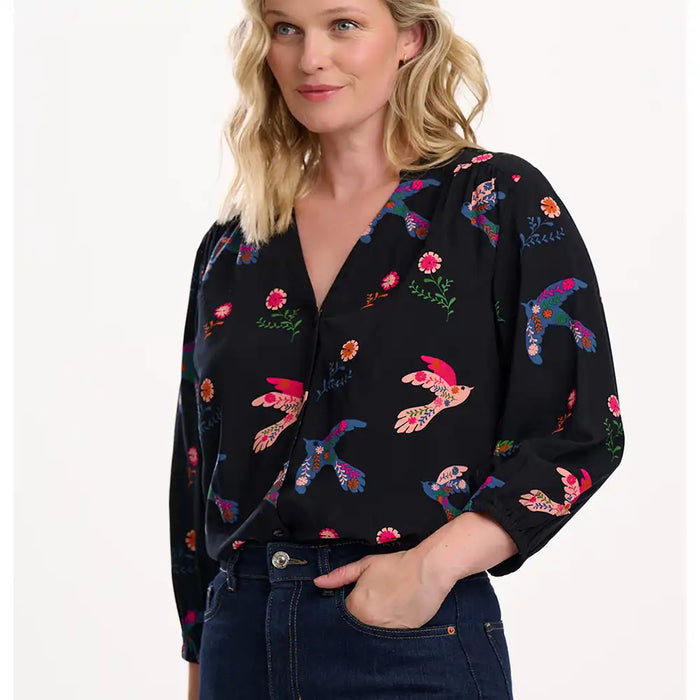 Woman wearing a black blouse with colorful bird patterns on a white background