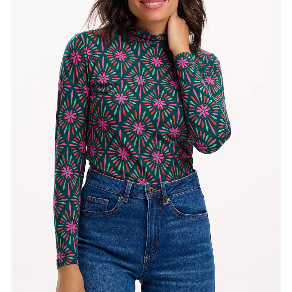 Woman wearing a green patterned long-sleeve top and blue jeans on a white background