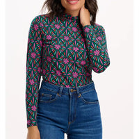 Woman wearing a green patterned long-sleeve top and blue jeans on a white background