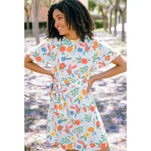 Woman wearing a floral dress standing in a garden with fallen flowers on the ground.