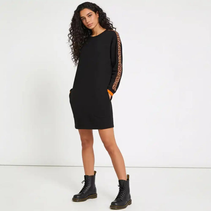 A woman modeling a black long-sleeve knit dress with leopard-print and orange patterned sleeve panels, paired with black combat boots, against a plain white studio background.