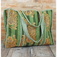 Green tote bag with tiger pattern on a wooden surface and brick wall background