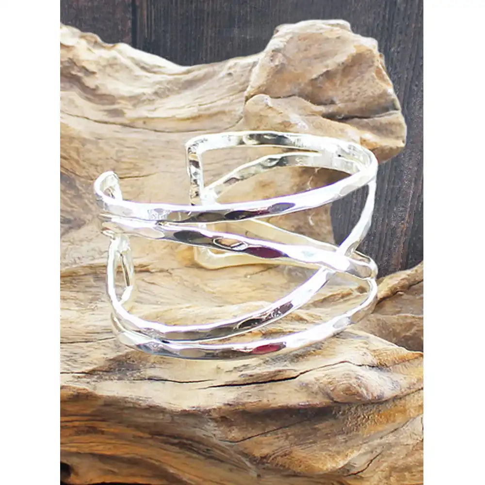 A polished silver wrap cuff bracelet displayed on a piece of natural driftwood against a dark wood background.