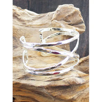 A polished silver wrap cuff bracelet displayed on a piece of natural driftwood against a dark wood background.